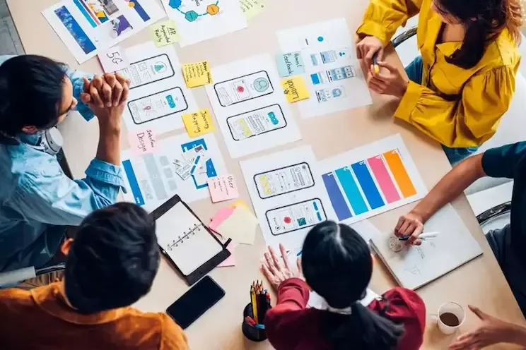 A team sketching website and app wireframes on paper around a table